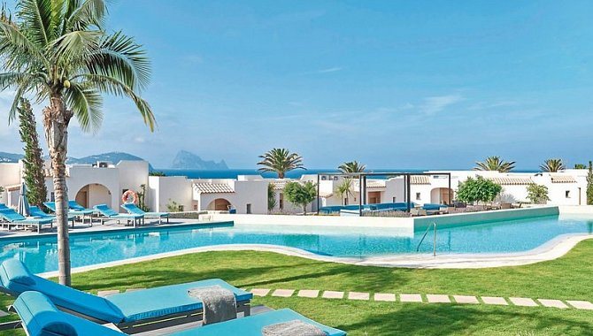 Poollandschaft mit weißen Villen, Palmen und Sonnenliegen in mediterraner Gartenanlage des 7Pines Resort Ibiza