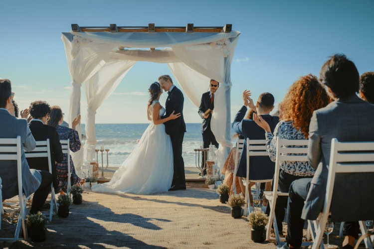 Paar steht unter Hochzeitsbogen vor den Gästen und Küsst sich