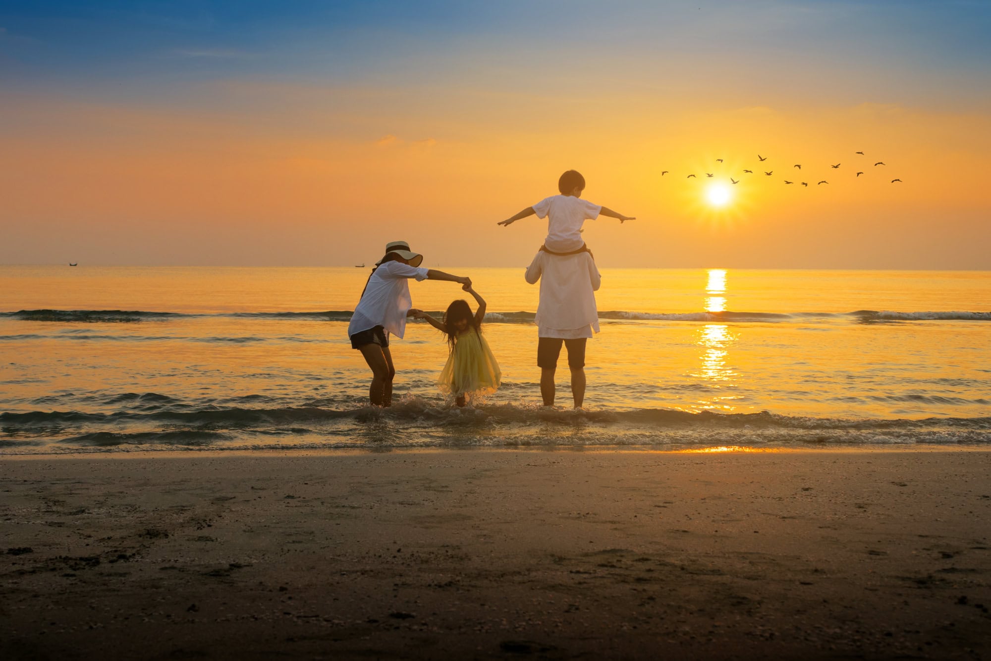 Eine Familie mit 2 Kindern spielt am Strand bei Sonnenuntergang