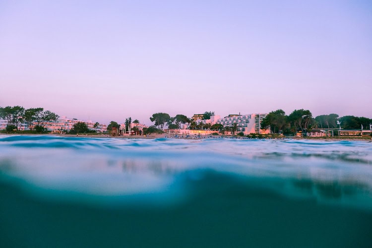 Strandhotels an einer Bucht bei Abenddämmerung, Blick knapp über der Wasseroberfläche.
