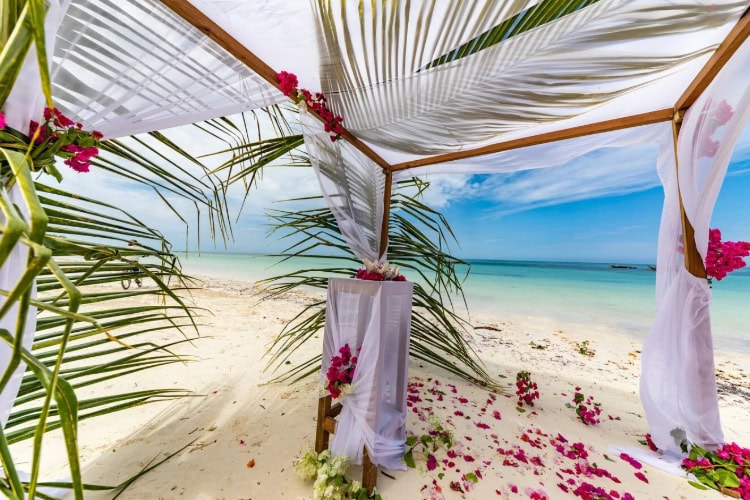 Hochzeitspavillion am Strand mit Blumen und Palmzweigen