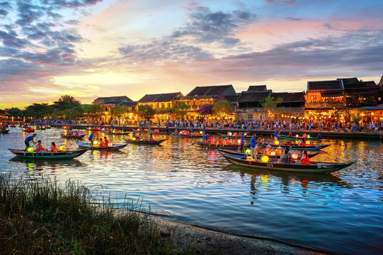 Traditionelle Boote mit bunten Laternen auf dem Fluss in Hoi An bei Sonnenuntergang, stimmungsvoll beleuchtet.
