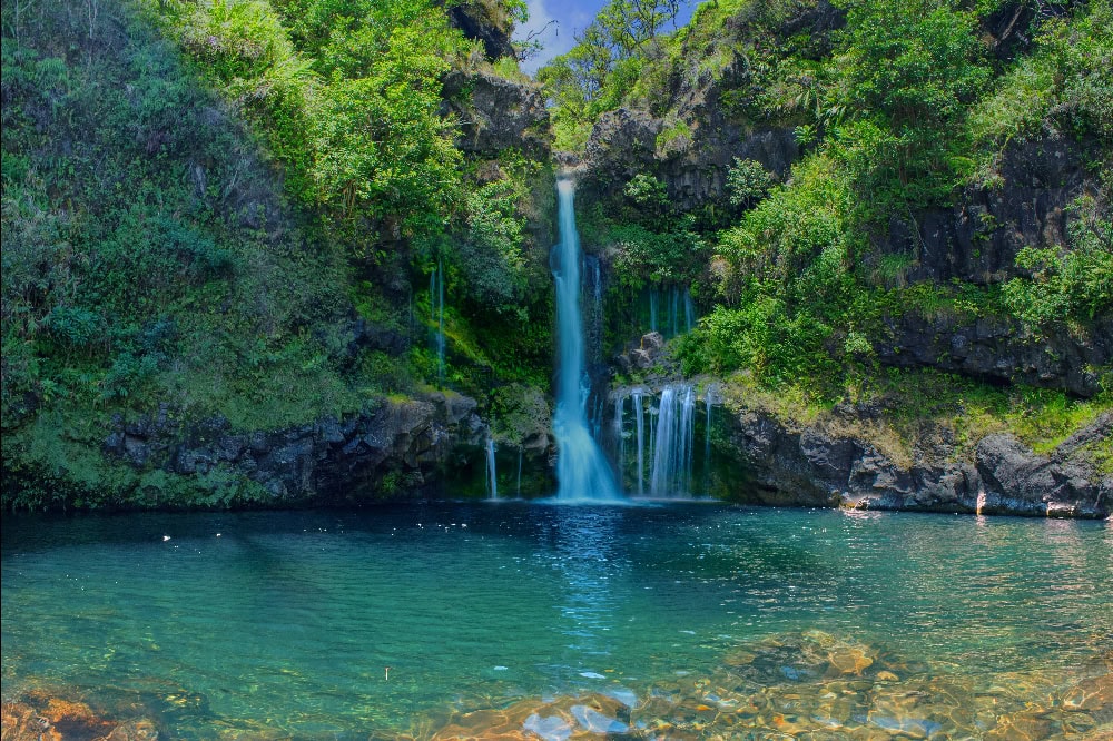 Idyllischer Wasserfall mit klarem Becken inmitten tropischer Vegetation auf Maui.