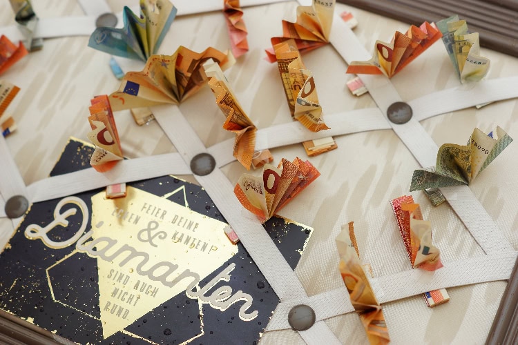 Kreatives Geldgeschenk mit gefalteten Geldscheinen in Schmetterlingsform, befestigt auf einem Bandgitter mit goldfarbener Karte.