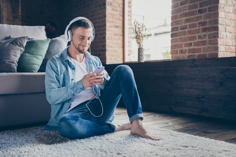 Ein Mann lehnt an einem Sofa und hört mit Kopfhörern Musik.