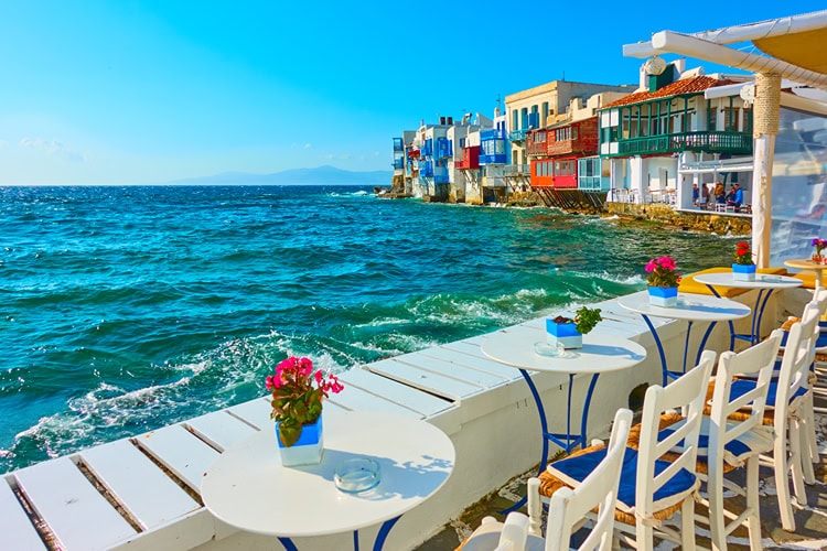 Tische mit Blumen am Meer in Mykonos' Viertel „Little Venice“ – bekannt für romantische Ausblicke und malerische Architektur.