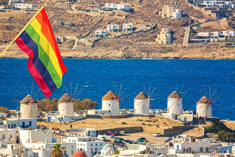 Regenbogenflagge weht über den ikonischen Windmühlen von Mykonos – Symbol für die LGBTQ+-freundliche Atmosphäre der Insel.