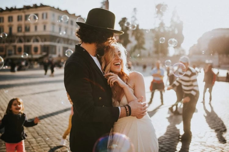 Hochzeitspaar steht auf einem Platz in der Stadt umringt von Seifenblasen und Kindern