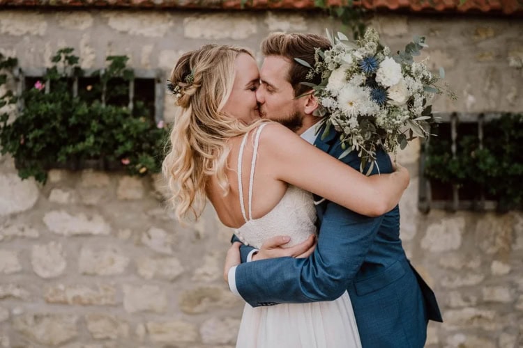 Hochzeitspaar küsst sich leidenschaftlich. Die Braut hält einen Brautstrauß